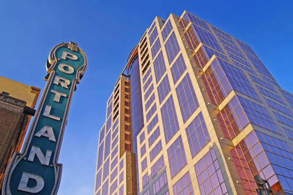View looking up at vintage neon PORTLAND sign and modern high-rise building in Portland, Oregon.